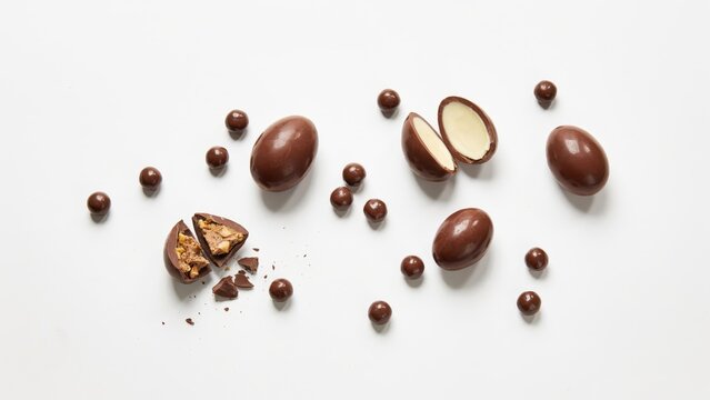 Delicious chocolate eggs and small round candies on white background