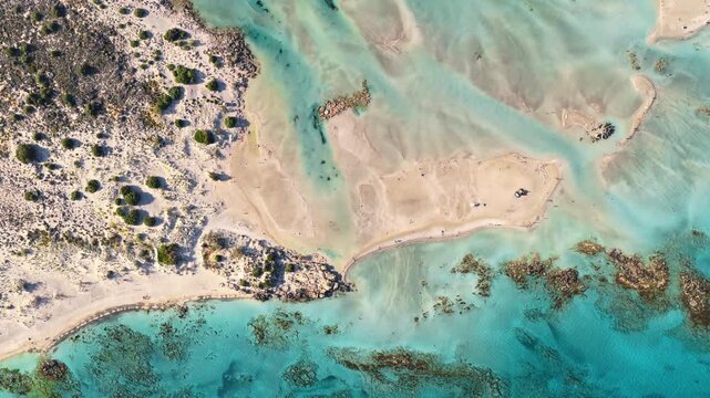 Overhead aerial drone view of low green dunes meeting a shallow turquoise lagoon with sandbars, Elafonissi, Greece