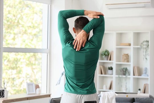 Sporty young man exercising at home, back view