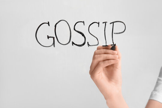 Woman writing word GOSSIP on glass against light background, closeup