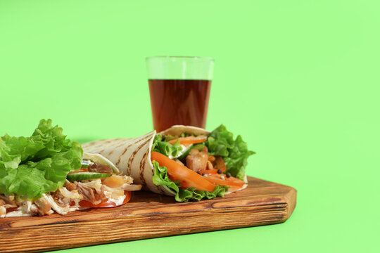 Board with tasty doner kebabs and drink on green background