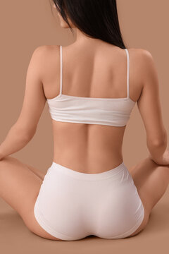 Beautiful young woman in white underwear sitting on brown background, back view