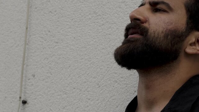 Thoughtful man with beard smoking cigarette near textured wall