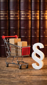 Miniature shopping cart with boxes and a paragraph symbol on a wooden table, signifying consumer law or legal purchase concepts.