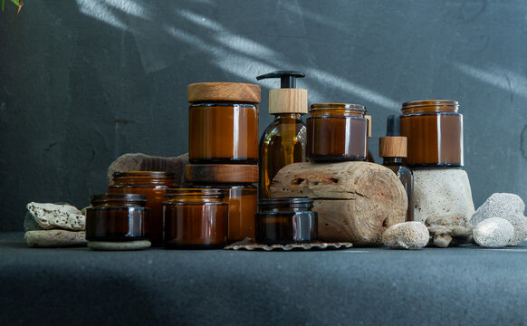 Eco-Friendly Amber Glass Cosmetic Jars and Bottles with Wooden Lids on Natural Stone and Wood Background.