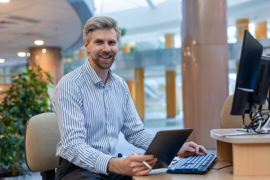 Happy smiling employee, young entrepreneur using digital tablet computer analyzing finance trading market data working standing in open space office
