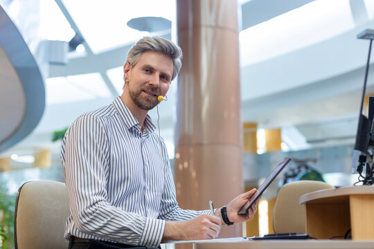 Happy smiling employee, young entrepreneur using digital tablet computer analyzing finance trading market data working standing in open space office