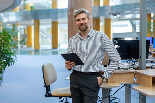 Modern business man in formalwear using digital tablet while standing in open space office