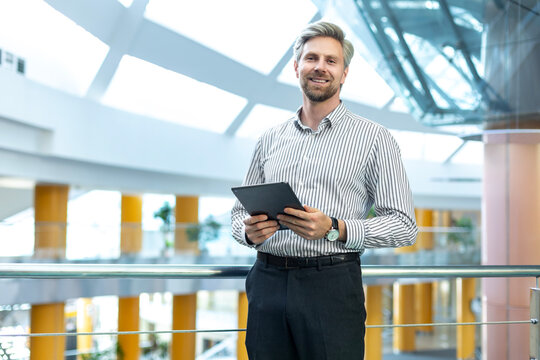 Modern business man in formalwear using digital tablet while standing in open space office