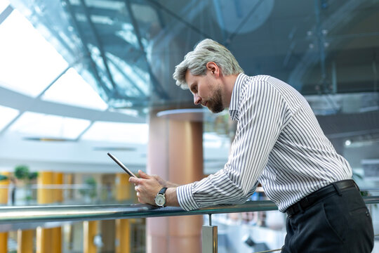 Modern business man in formalwear using digital tablet while standing in open space office