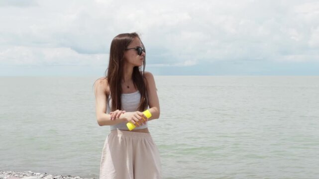 teenage traveler spreads sunscreen on her arm while standing on a pebble beach, highlighting sun care, heat safety, healthy summer habits and protection during seaside