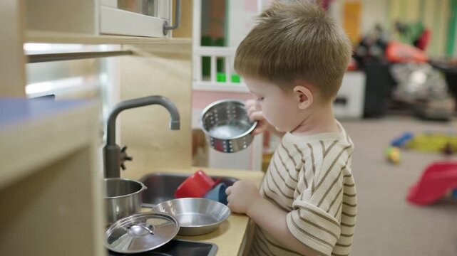 Focused toddler child washing dishes at kids club play kitchen