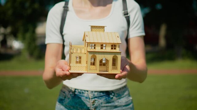 Property sale concept with wooden house extended toward buyer. Mortgage financing and affordable housing offer with new residence investment planning. Real estate agency presentation and dream home