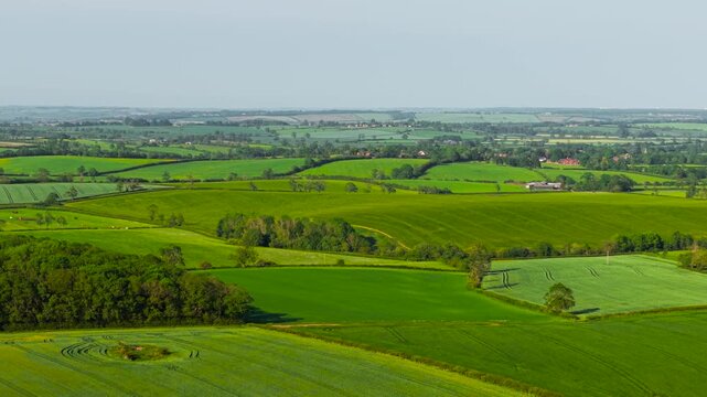 Aerial farmland countryside crop fields spring. Rolling agricultural landscape covering green rural hills under clear daytime weather. Fresh cereal crops and patchwork farming scenery extending across
