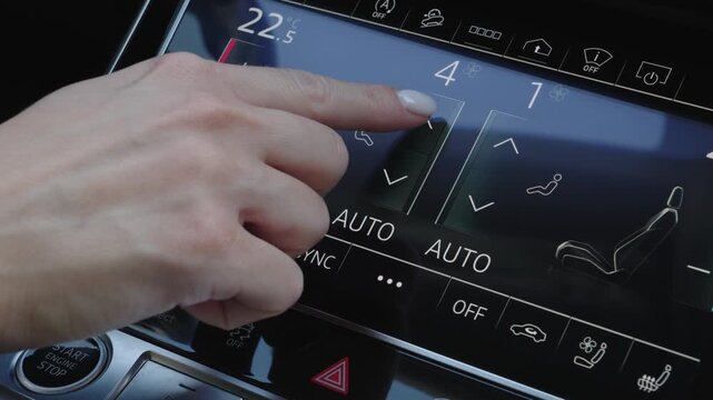 Close-up of female hand touching screen to change climate control fan intensity and airflow settings inside modern luxury vehicle.