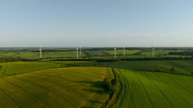 Renewable electricity flowing from wind farm across patchwork rural fields. Clean energy production supporting sustainable infrastructure and ecological balance. Wind turbines contributing renewable