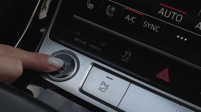 Close-up of female hand pressing start engine stop button on modern luxury car console panel to turn on vehicle.