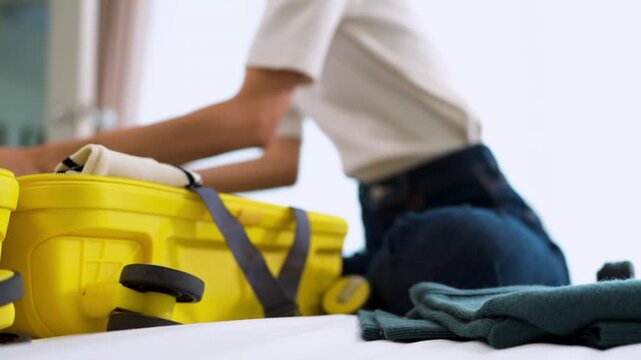 Close-up of Asian woman hands packing casual clothes and headphones into a suitcase. Concept of travel preparation, luggage organization, holiday planning and modern lifestyle.