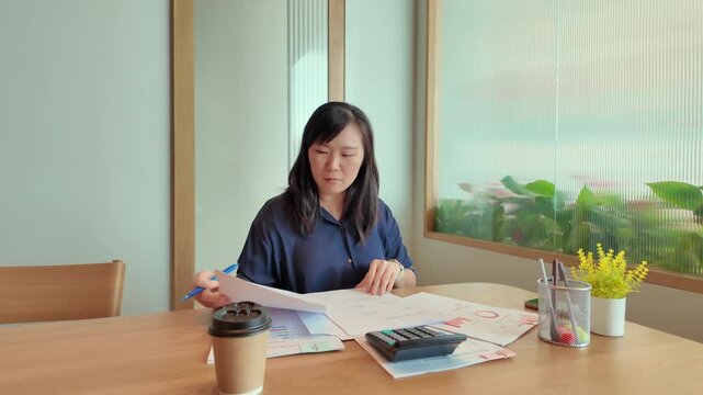 A business professional reviewing financial reports with calculator, documents, smartphone, and coffee on a wooden office desk.