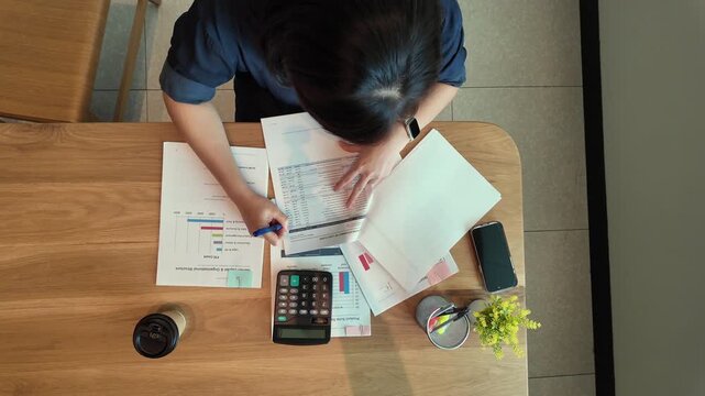 A business professional reviewing financial reports with calculator, documents, smartphone, and coffee on a wooden office desk.