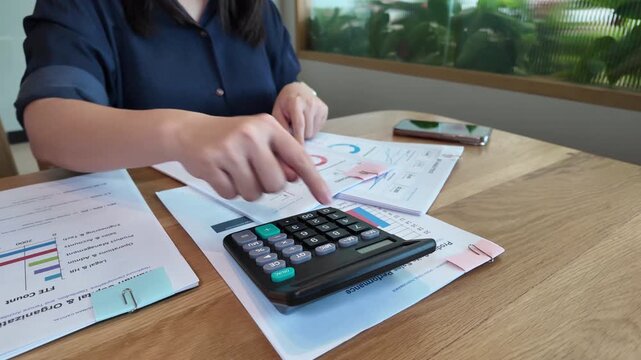 A business professional reviewing financial reports with calculator, documents, smartphone, and coffee on a wooden office desk.