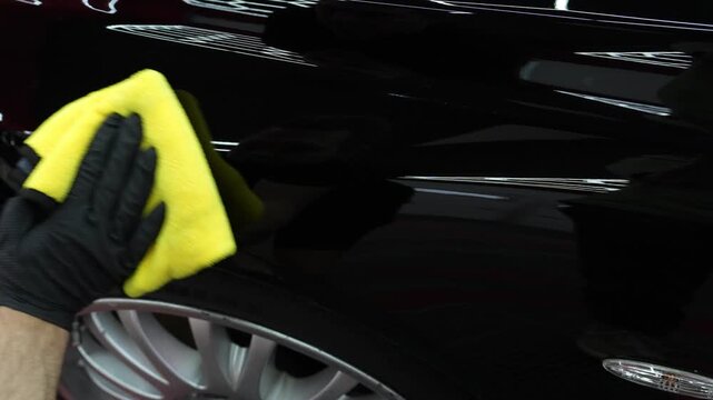 Vehicle detailing and paint correction process. 4K video of removing polishing paste with a microfiber towel to reveal deep gloss on black paint