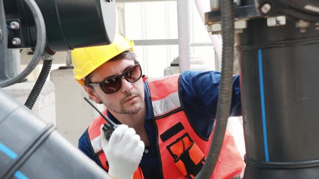 Male technician inspects the coolant inlet and outlet pipes of the cooling tower checks the flange connections and reports walkie talkie engine room while testing the cooling system.