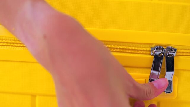 Close-up of Asian female hand pulling a zipper to close a bright yellow suitcase. Concept of packing luggage, travel preparation and upcoming holiday vacation.