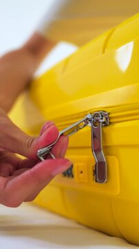 Close-up of Asian female hand pulling a zipper to close a bright yellow suitcase. Concept of packing luggage, travel preparation and upcoming holiday vacation. Vertical Shot