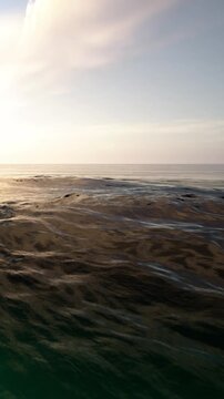 The sun sets over the ocean, casting light on the water. Waves are rolling in softly. The horizon is visible, blending sea and sky as evening approaches.