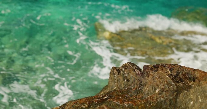 Clear Turquoise Ocean Water with Gentle Waves Lapping Against Rugged Coastal Rocks, Showcasing the Serene Beauty of a Sunny Tropical Shoreline.