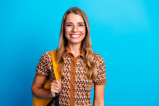 Young smiling female student with glasses and yellow bag against blue background