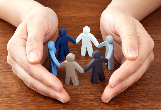 Hands protecting a circle of colorful figurines symbolizing unity and teamwork together in harmony