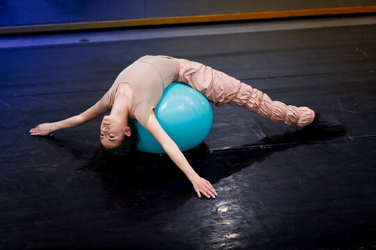 Dancer performs an exercise routine on a blue stability ball in a studio during a training session in the afternoon