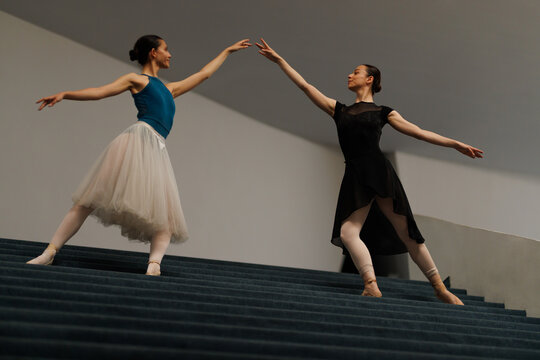 Two ballet dancers performing a graceful pas de deux on a modern staircase, pointe shoes and tutus creating elegant lines and poised movement in a minimalist architectural setting