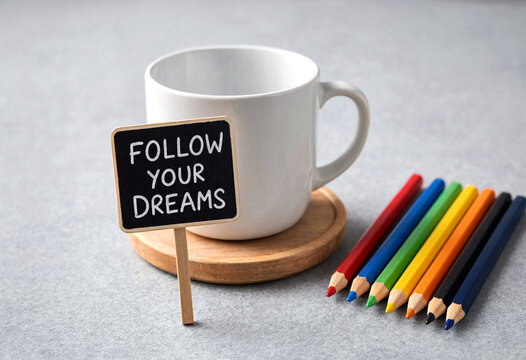 Follow your dreams sign with a white coffee cup and colorful pencils on table
