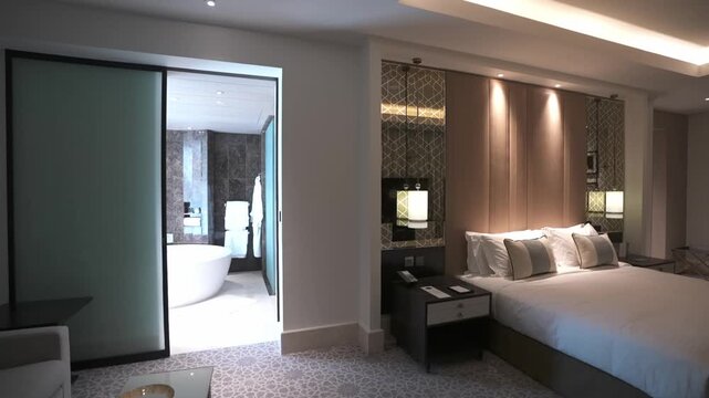 Luxury hotel suite master bedroom view facing an open glass sliding door leading into a modern bathroom layout.