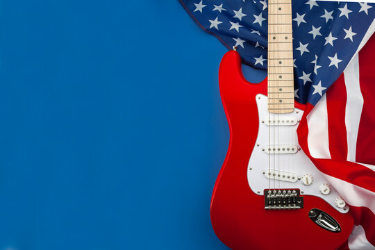Red electric guitar with American flag on blue background. Patriotic music concept inspired by rock culture, live performance and American entertainment with copy space