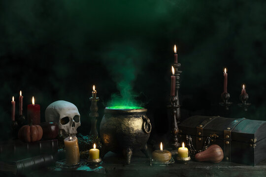 Halloween background, witch's cauldron with boiling magic potion, candles, pumpkins, skull on the table.