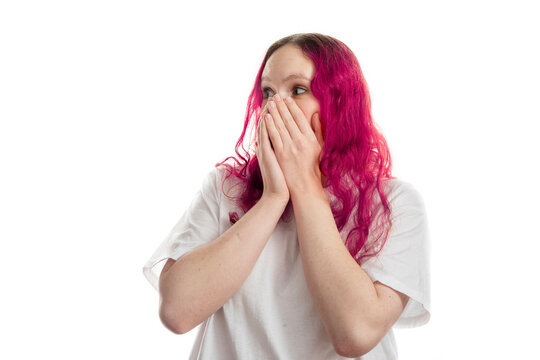 Portrait of a young woman with pink hair covering her mouth, reacting to bad news with worry and anxiety. Isolated on white background, concept of stress and uncertainty.
