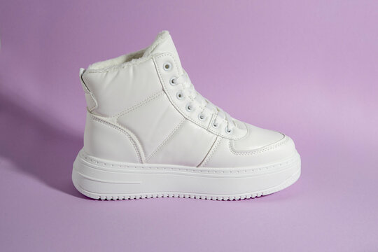 White winter platform sneakers on pastel purple background, casual cold season footwear photographed in minimalist studio style
