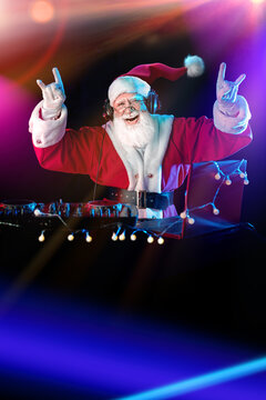 DJ Santa Claus mixing tracks in a nightclub at a Christmas and New Year party or Corporate events. Senior disc jockey as Santa listening music, headphones, laptop, mixer controller player, turntable