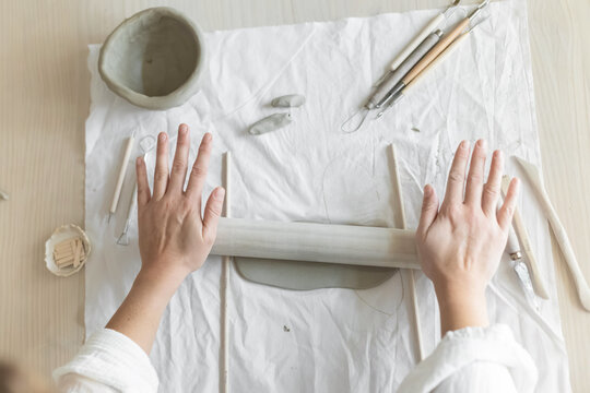 Women artist pottery shaping clay on a worktable with tools and cloth