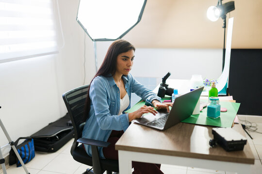Female product photographer working on laptop in a professional studio, managing digital assets and creative workflow