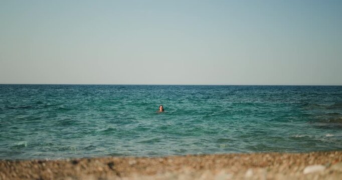 A person enjoys a refreshing swim in the vast, clear blue ocean, with gentle waves rippling under a bright summer sky, creating a serene and peaceful vacation scene.