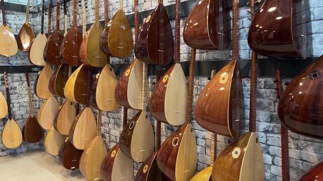 Collection of traditional string instruments displayed on a wall, showcasing various shapes and colors in a well-lit music shop setting with a brick background