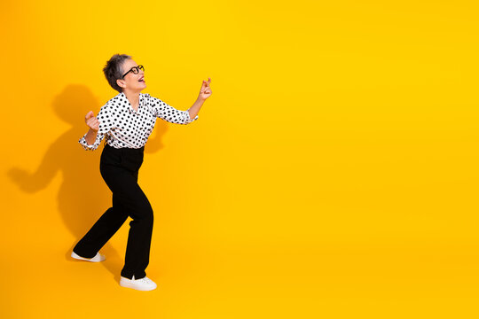 Happy mature businesswoman in polka dot blouse dancing against a vibrant yellow background