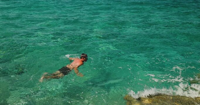 A Man Swims with Goggles in Crystal Clear Turquoise Ocean Water, Enjoying a Refreshing Summer Vacation on a Sunny Day.