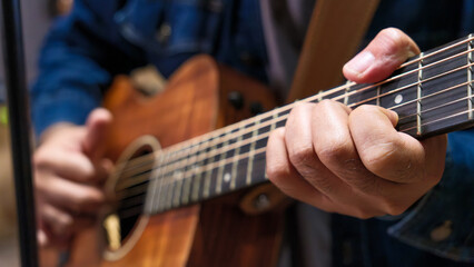 Fototapeta premium Close-up of professional asian male musician is happy singing and playing acoustic guitar while at music studio. Positive musician enjoy instrumental music. Skill and practice, enjoyment and relax.
