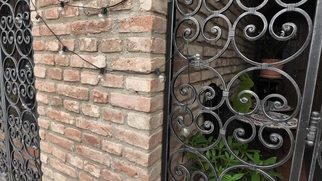 Ornate wrought iron gate with brick wall and potted plants, elegant entryway detail